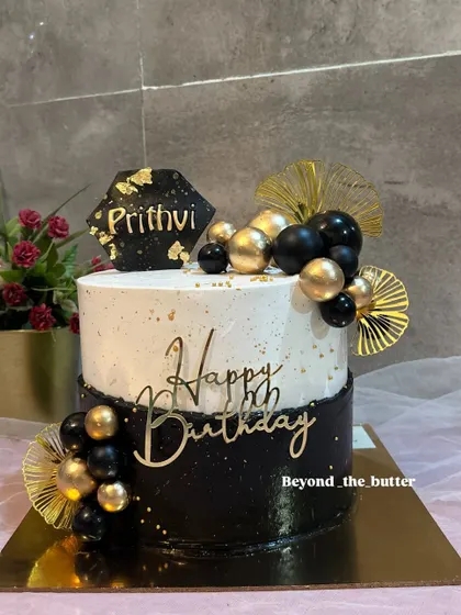 A sophisticated black, white, and gold birthday cake. The modern design with balloon toppers is perfect for a stylish celebration.