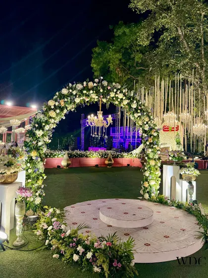 A beautiful floral archway that served as a photo point. The arch is covered in white and pastel flowers, with a chandelier hanging in the middle, creating a perfect frame for pictures.