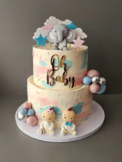 Oh Baby! A two-tier baby shower cake in pastel pink and blue. This cake is perfect for a gender reveal party, decorated with cute baby figurines and an elephant topper.