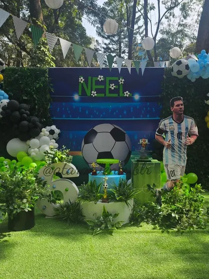 The main stage for a soccer-themed 6th birthday. The setup includes a backdrop with a giant soccer ball, a life-sized cutout of Lionel Messi, and a lush green turf floor.