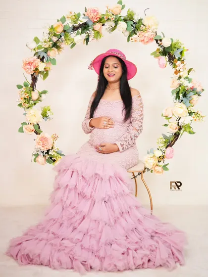 Pretty in pink. This mom-to-be is seated in our floral hoop, wearing a lovely lace and tulle gown and a stylish pink hat for a chic and feminine portrait.