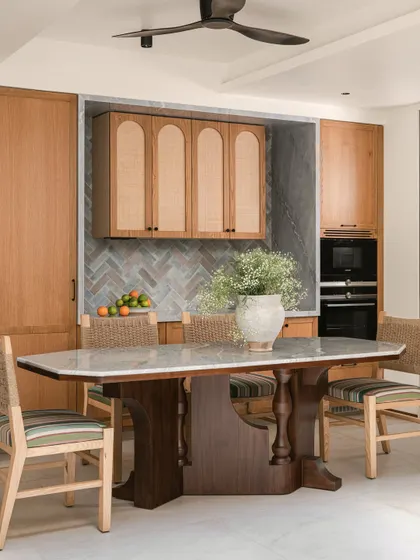The dining and kitchen area in Kolam Pop is a celebration of craftsmanship and color. The sculptural dining table is paired with mint-green kitchen cabinets and a herringbone tile backsplash.