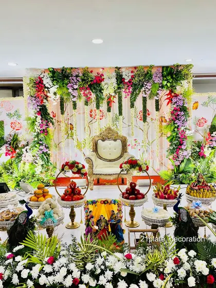 A beautiful and refreshing baby shower setup with a garden theme. The backdrop is printed with floral motifs and adorned with fresh flower garlands, creating a light and airy feel.