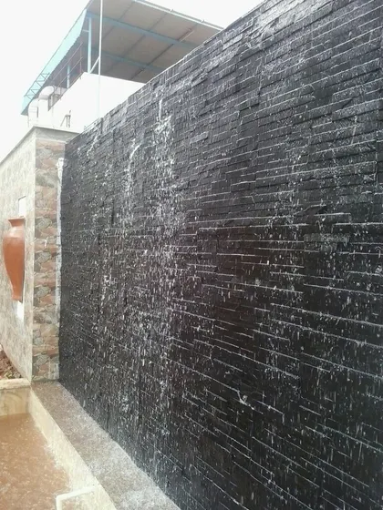 A modern waterfall feature made of stacked black slate tiles, with water flowing down the textured surface into a basin below. This creates a dramatic and contemporary look.