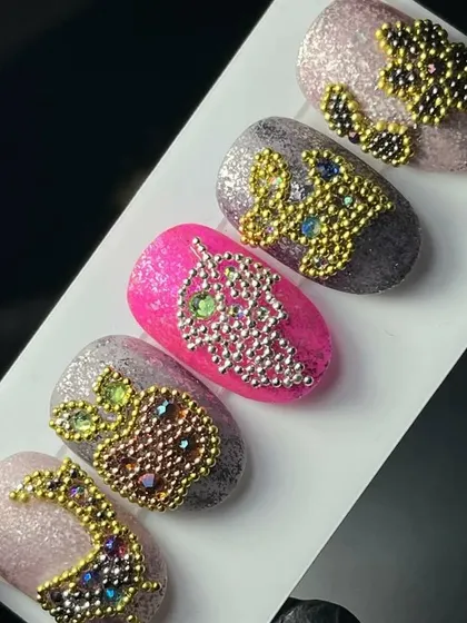 A collection of magical crystal nail art, where tiny beads are used to form shapes like pineapples and grapes on a glittery base.
