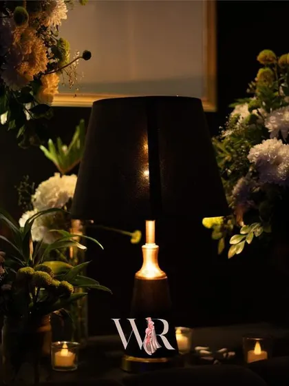 A detail of the ambient lighting, with a soft, dark lampshade surrounded by arrangements of white flowers. This creates a moody, intimate atmosphere perfect for a lounge area.