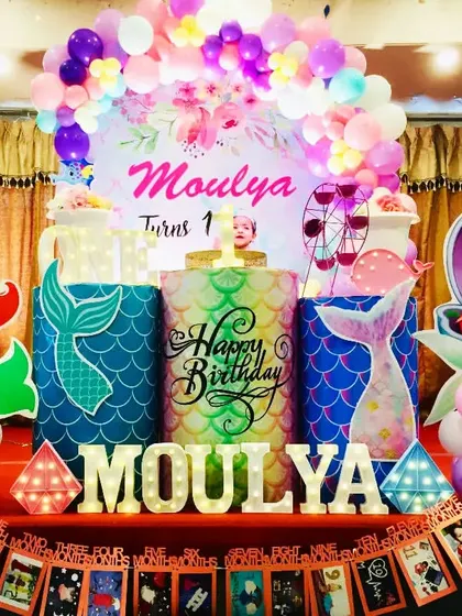 An under-the-sea adventure with a Little Mermaid theme for Moulya's first birthday. The setup includes Ariel cutouts, mermaid tail patterns, and a custom photo banner.