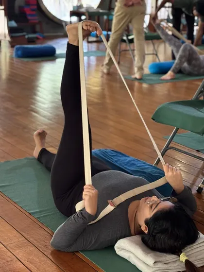 The yoga belt is a simple but powerful tool. Here, it is used to help a student in Supta Padangusthasana, ensuring the leg can be extended without straining the back, teaching the correct action of the hip joint.