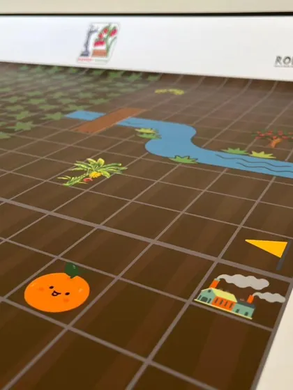 This section of the Explorers mat shows various illustrated elements like a river and an orange, creating a fun and engaging story for the young coders to follow.