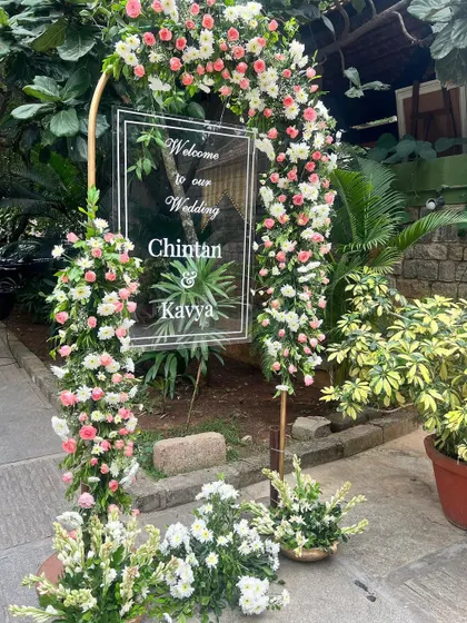 A personalized welcome sign for Chintan and Kavya's wedding, framed by a beautiful arch of pink and white flowers.