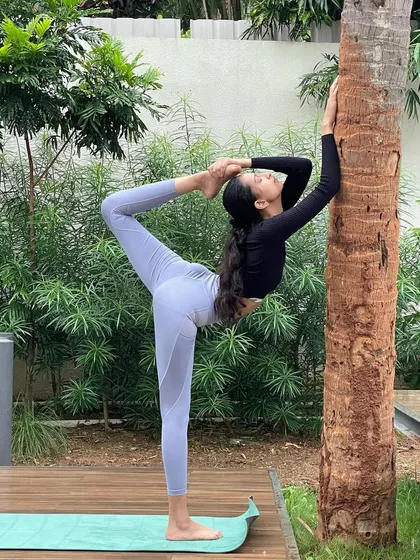 Using a tree for support while practicing a deep stretch in Natarajasana (Dancer's Pose). Taking support is a smart way to work on balance and alignment in challenging poses.