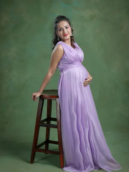 A glamorous studio portrait of a mom-to-be in a flowing lavender gown. Leaning against a stool, she looks like a goddess, full of grace and beauty.