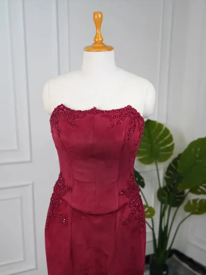 A detailed shot of the strapless corset bodice on the red suede dress, showing the scalloped neckline and intricate creeper embroidery.