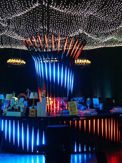 The central bar is a masterpiece of light and design. The illuminated base and a canopy of fairy lights create a vibrant hub for the celebration.