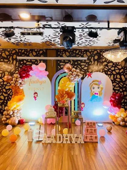 A princess-themed birthday decoration for "Aadhya". This setup uses custom arch backdrops, one with a princess illustration, and a warm-toned balloon arrangement in rose gold, orange, and pink.