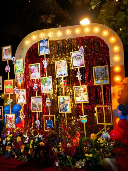A memory wall at a carnival-themed party. Photos of the birthday child are displayed on a shimmering red backdrop, creating a personal and heartwarming focal point.