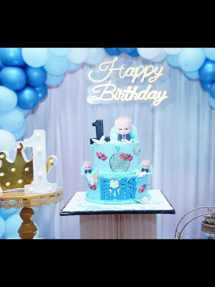 A Boss Baby cake in front of a blue and white balloon arch, ready for the first birthday celebration.