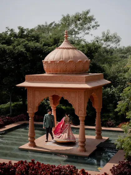 A wide shot of the couple in front of a traditional Indian gazebo set in a pool of water, showcasing a unique and grand pre-wedding location.