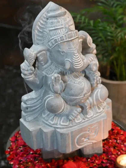 A stone Ganesha statue, with incense smoke gently rising, placed on a bed of flowers. This image captures the essence of 'Kai kelasa', the inherited skill of our stone carvers who visualize and create such beautiful art.