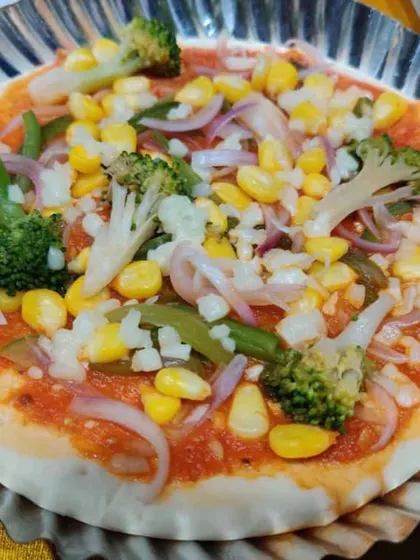 A pizza base topped with my homemade sauce and fresh vegetables like broccoli, corn, and onions, ready for the oven.