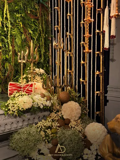 The sacred space for the ceremony, with trishuls, a damru, and coconuts arranged amidst a bed of white flowers against a green wall.