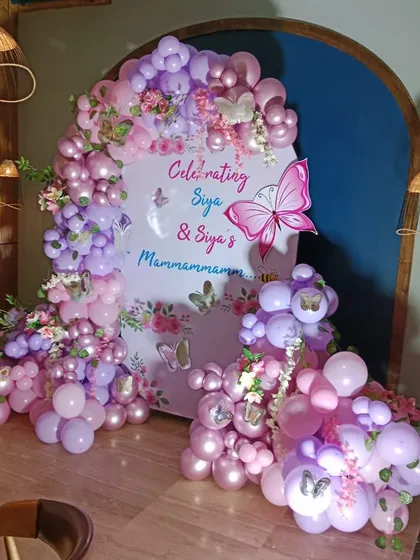 An elaborate butterfly-themed celebration with a custom arched backdrop and a lush balloon garland in shades of pink and purple.