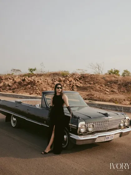 A full-length portrait showcasing her elegant black dress against the classic lines of the vintage car. This shot from the Goa pre-wedding session is all about timeless style and sophistication.