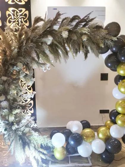 A unique and rustic balloon arch made with pampas grass and a black, white, and gold balloon arrangement.