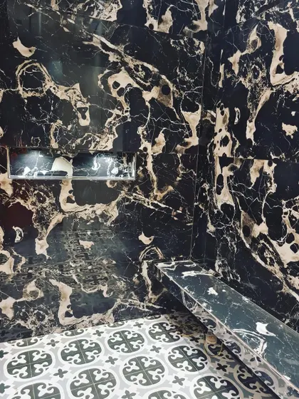 A shower designed with a built-in bench and niche, using dramatic black and gold marble. This is a perfect example of how to combine luxury with practical comfort.