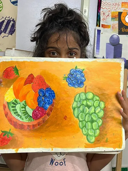 A proud student displays her vibrant fruit painting. This piece demonstrates a great understanding of color, composition, and how to render different textures using acrylics.
