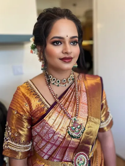 A classic South Indian bridal look with a beautiful gold and maroon saree. The eye makeup is a soft smokey brown with a touch of shimmer, paired with a bold lip for a timeless feel.