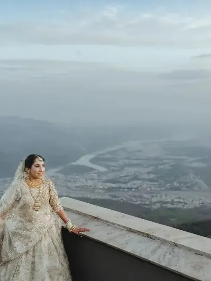A breathtaking wide-angle shot of the bride on a terrace, with a vast river and valley below, showcasing the epic scale of the location.