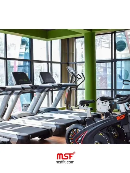 A wide shot of a cardio area equipped with our treadmills and spin bikes, set against a bright, windowed backdrop.