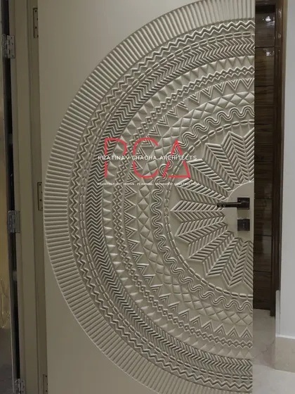 The intricately carved main door of The Cursive Abode, shown partially open to reveal the home's interior.