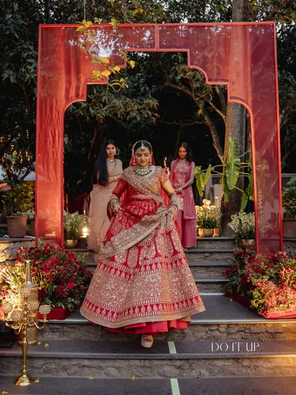 The bride's entrance, framed by a simple red arch that complements the traditional theme. The design focuses on creating impactful moments throughout the wedding experience.