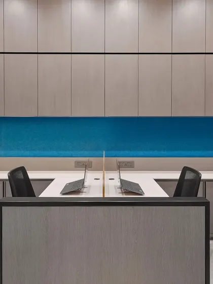 A clean and organized workstation setup with a calming blue backdrop. The design prioritizes functionality with built-in overhead storage and an uncluttered desk surface.