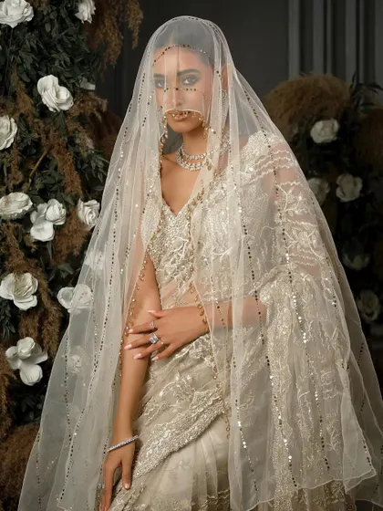 A full-length view of this stunning ivory saree by Nitika Gujral. The model is shrouded in a delicate, sequined veil, creating a mysterious and utterly romantic bridal portrait.