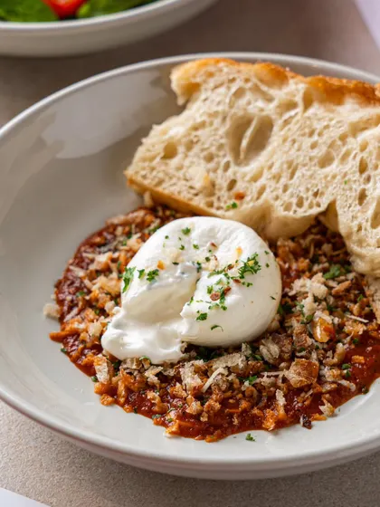 Burrata served over a savory tomato base with a slice of crusty bread. This image focuses on the creamy texture of the cheese and the rustic presentation.