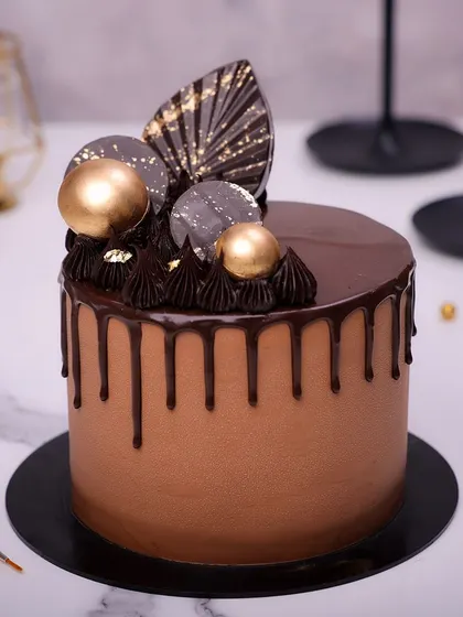 We indulge the senses with this elegant chocolate drip cake. A rich chocolate cake is topped with a fan of decorative chocolate, gold spheres, and delicate gold leaf accents, making it a sophisticated and decadent choice for Father's Day.