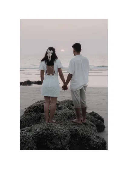 A beautiful shot from behind, showing the couple holding hands and watching the sunset. The bow in her hair adds a sweet, romantic detail.
