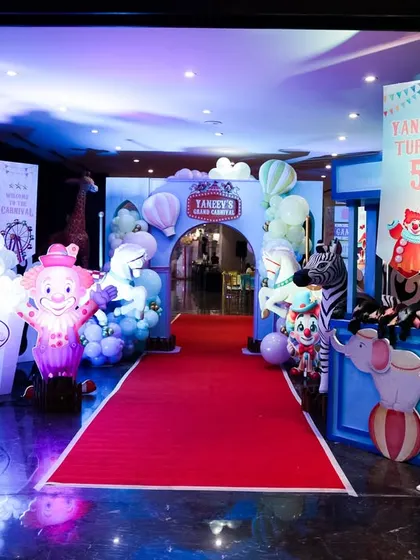 A night view of the grand carnival entrance, with dramatic lighting highlighting the red carpet and clown decorations.