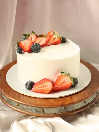 A clean, minimalist cake topped with fresh strawberries and blueberries. The fruit is the star here.