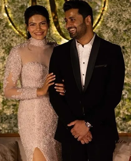 A happy couple posing in front of an elegant all-white floral wall at their reception. The custom monogram adds a personal touch to the sophisticated and modern decor.