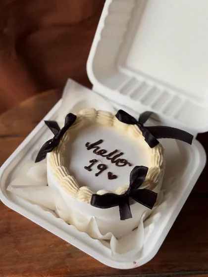 A chic, Pinterest-inspired bento cake for a 19th birthday. The design is simple and elegant, with "hello 19" written on a white cake adorned with four black satin bows.