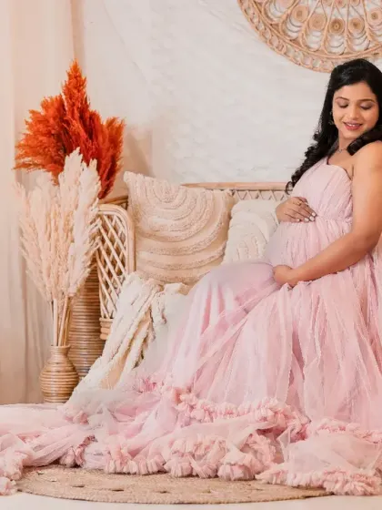 Serenity and style. The mom-to-be is seated gracefully on a rattan couch, her flowing pink gown cascading around her, surrounded by pampas grass for a perfect boho vibe.