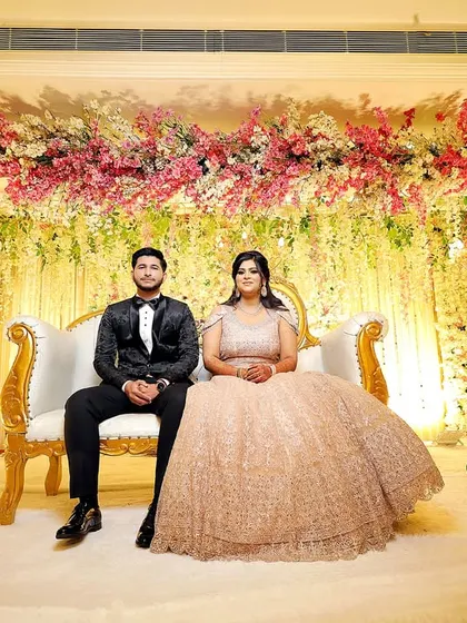 The couple seated on a grand stage, surrounded by a stunning floral arrangement. This captures the scale and beauty of their engagement celebration.
