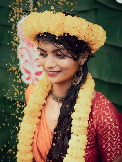 A lovely portrait of a bride during her Haldi ceremony, adorned with floral jewelry and smiling as she is showered with petals.