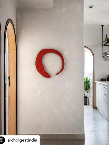 A bold red art piece, representing the 'Red Circle of Fate', adds a pop of color and a deeply personal story to the minimalist 'Unmei' home. It stands out against the lime-washed walls, symbolizing the clients' journey.