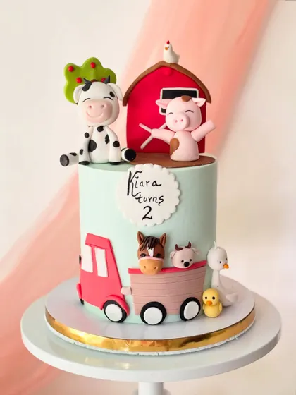 A fun farm-themed cake for a second birthday. It features a cow, pig, horse, and duck, with a red barn and tractor to complete the scene.