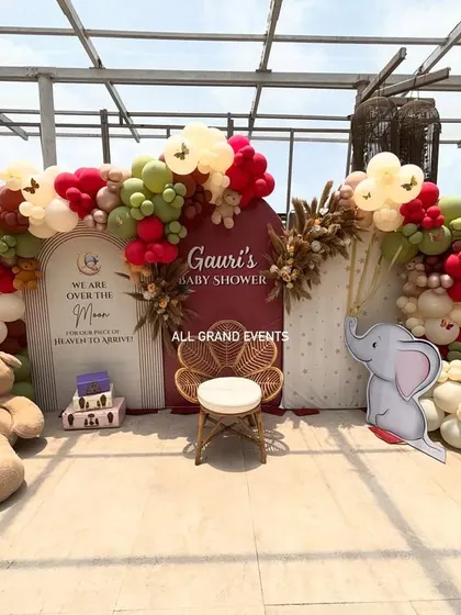 I create beautiful and memorable setups for milestones like baby showers. This 'Over the Moon' theme includes a custom backdrop, an elegant balloon arch in earthy tones, and adorable props like teddy bears and a wicker peacock chair for the mom-to-be.